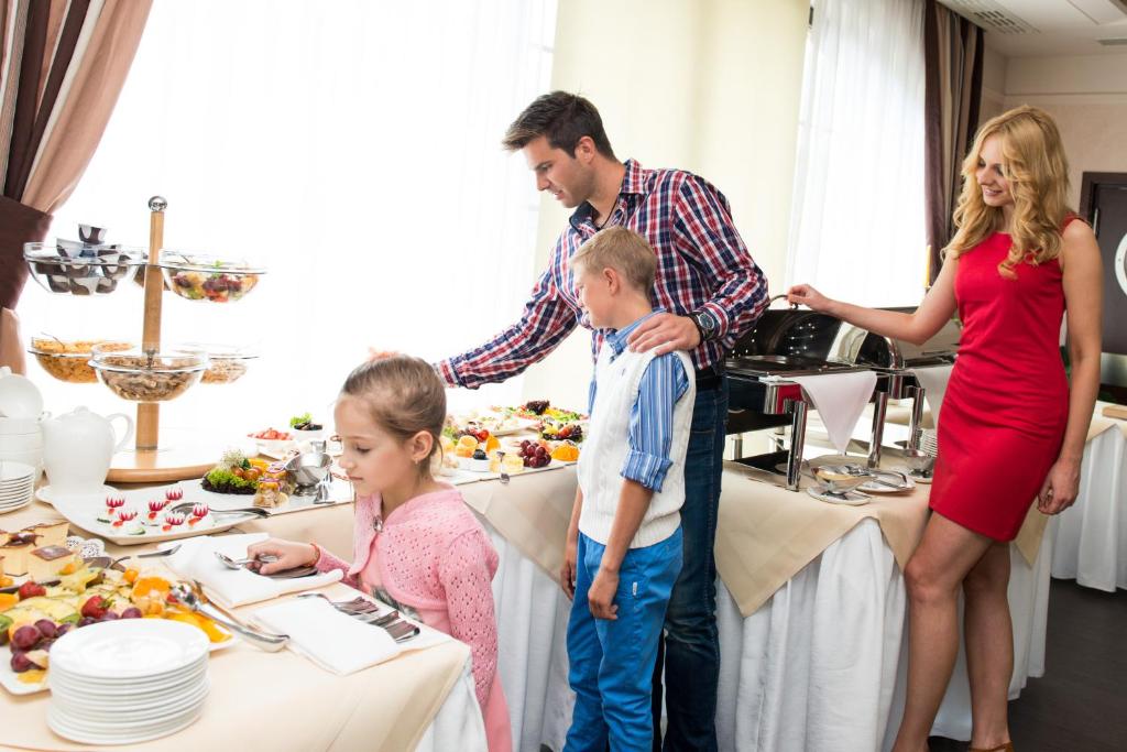 Family selecting food at buffet table, father helping children while woman in red watches.