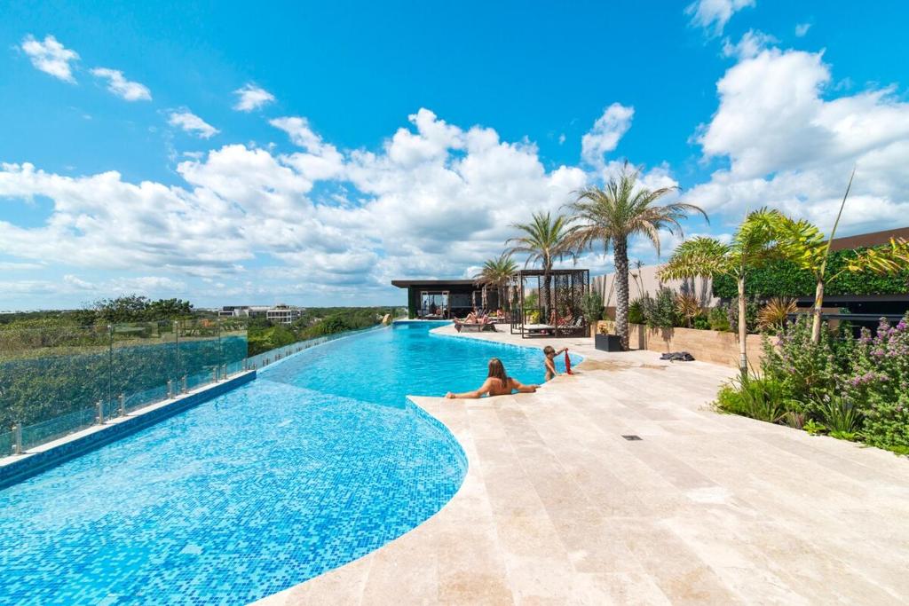 Una piscina con gente sentada en el borde. en Vibra Bonito - Boho Chic Studio with Rooftop & Infinite Pool, en Tulum