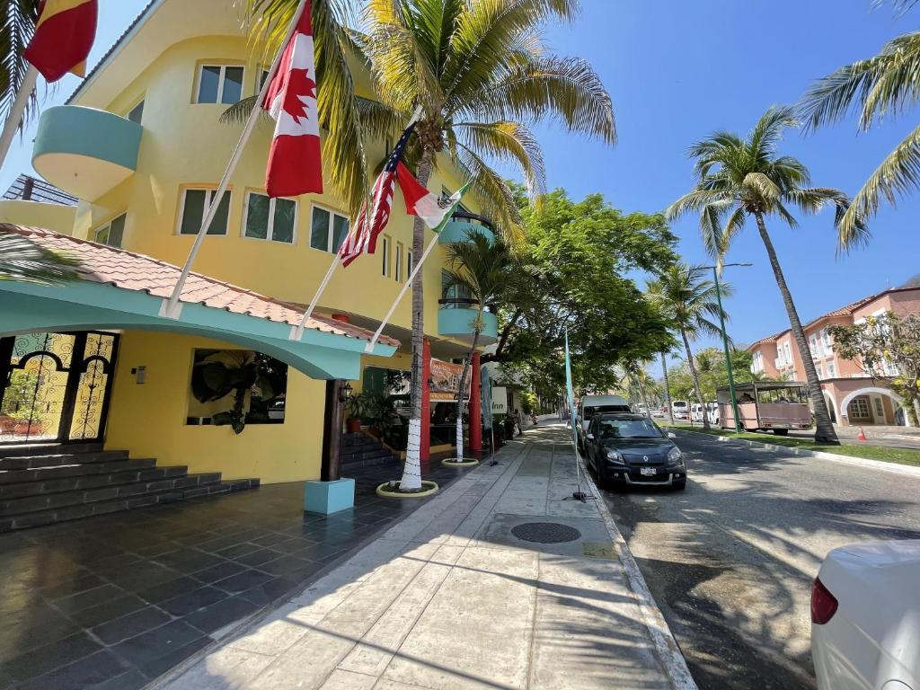 a street with palm trees and a yellow building with flags at Real Marina Blue 102B - Santa Cruz in Santa Cruz Huatulco