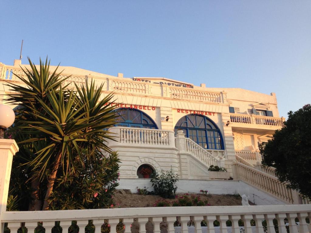 a large white building with a palm tree in front of it at Parthenon in Ios Chora