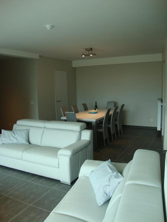 ein Wohnzimmer mit weißen Sofas und einem Tisch mit Stühlen in der Unterkunft Karthuizer Zeezicht I in Nieuwpoort