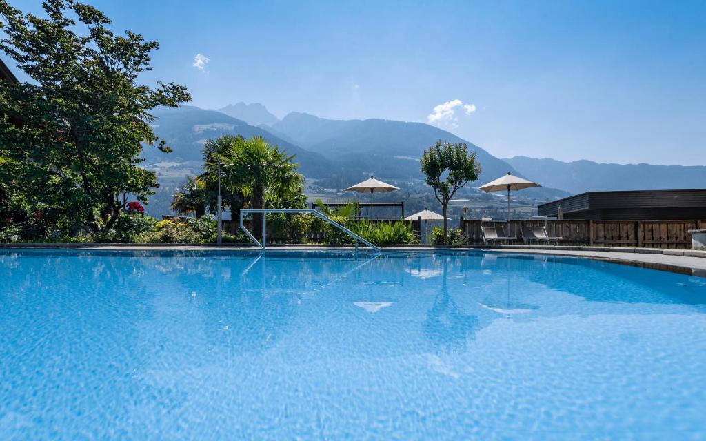 a large blue swimming pool with mountains in the background at Hotel Zirmerhof & Residence in Rifiano