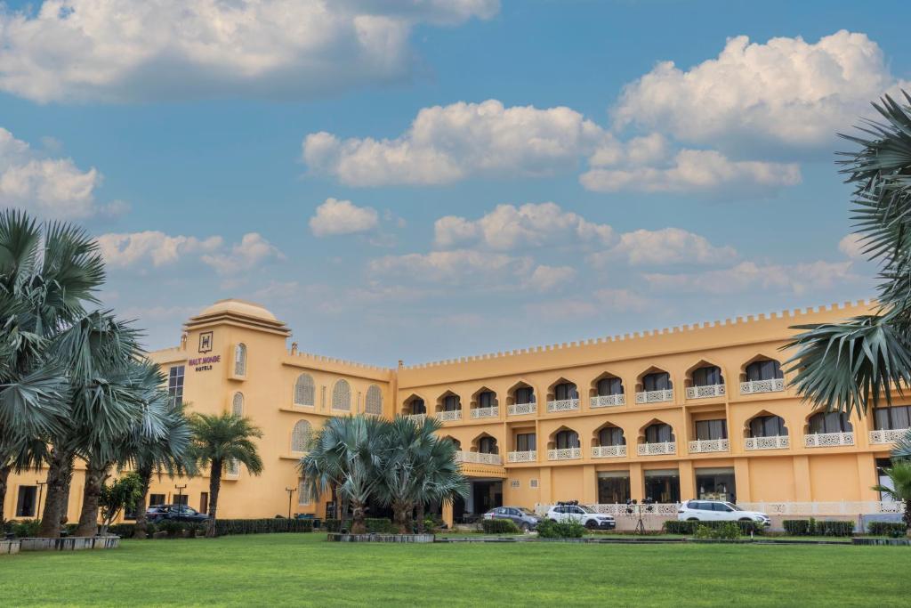 a large yellow building with palm trees in front of it at Haut Monde Rajputana Palace in Behror