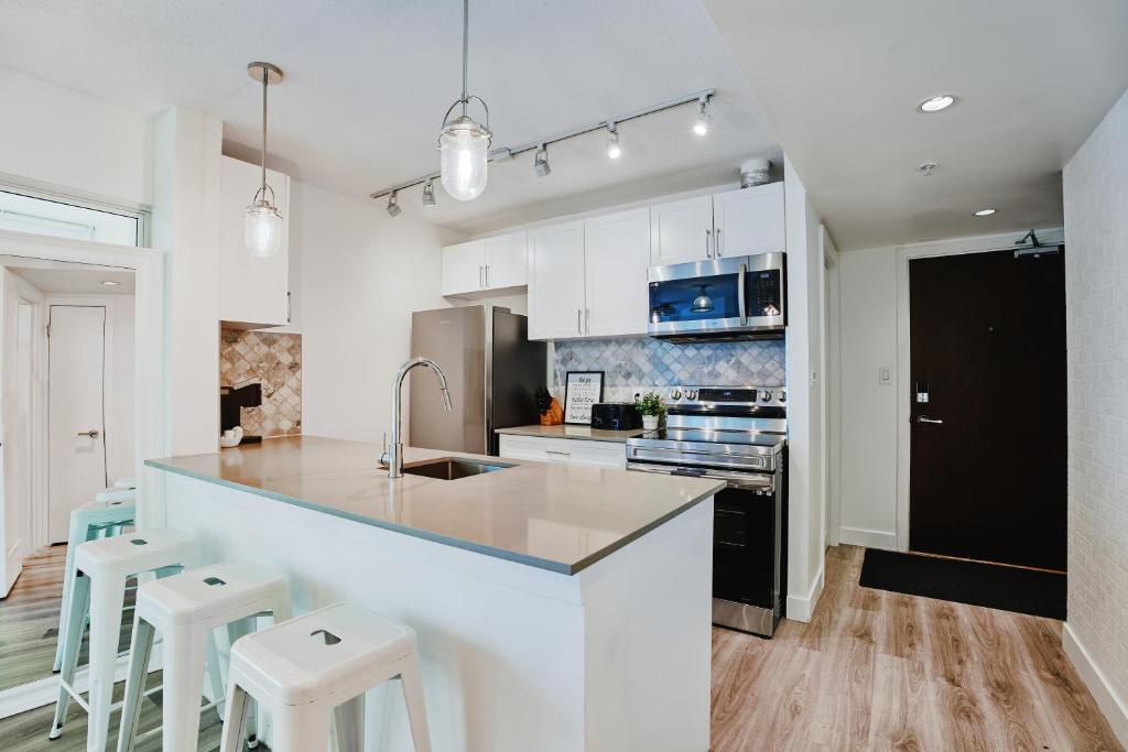 a kitchen with white cabinets and a counter with stools at Cozy Urban Living! 2 mins from BC place, private parking ! in Vancouver