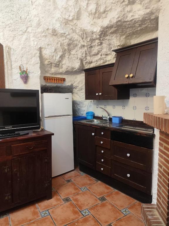 Una cocina con gabinetes de madera y un refrigerador blanco. en Cueva del castillo de Chinchilla, en Chinchilla de Montearagón