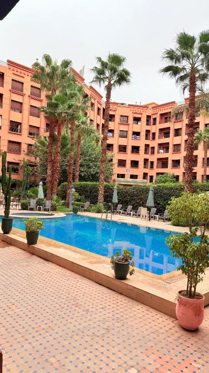 a swimming pool with palm trees and a large building at Appartement 6 personnes piscine hivernage Marrakech in Marrakesh