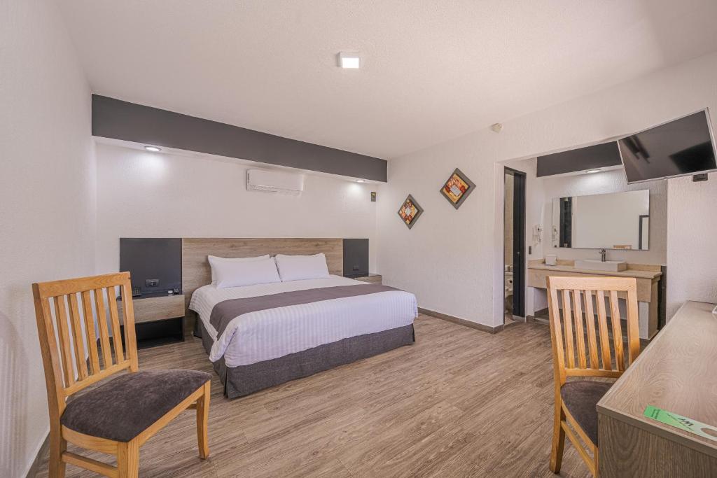 a bedroom with a bed and two chairs and a television at Hotel Malibu in Guadalajara