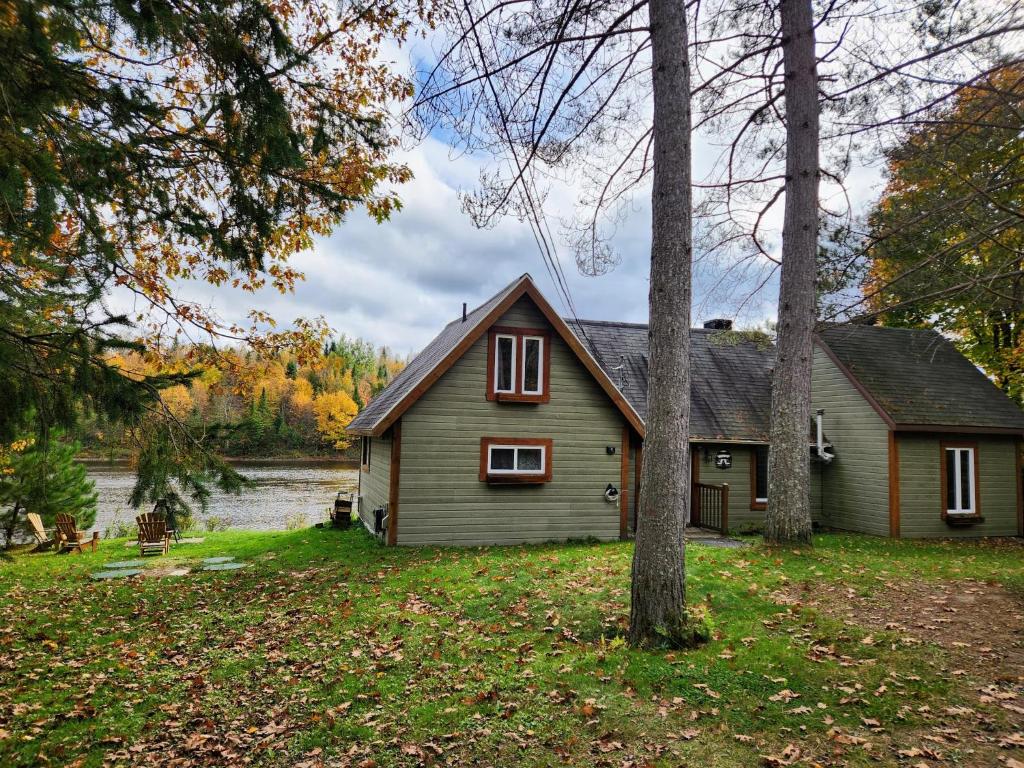 a house sitting next to a river with trees at Chalet L'Apéro des Chutes - Spa, détente & nature au bord de l'eau en Mauricie in  Notre-Dame de Montauban