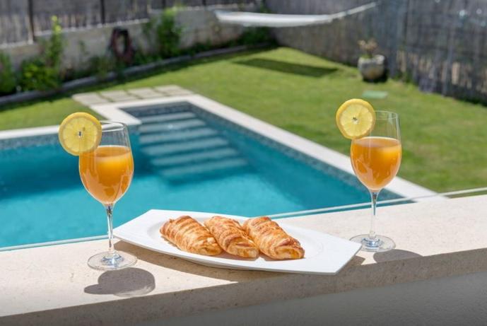 two glasses of orange juice and croissants on a table near a pool at Luxury Apartment with Heating Pool in Šibenik