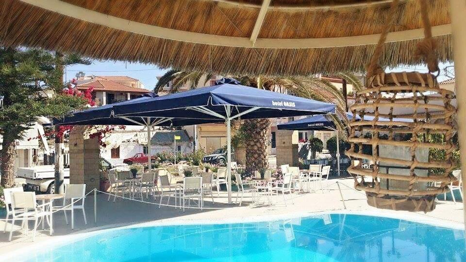 a swimming pool with a blue umbrella and chairs and a table and chairs at Oasis Hotel in Skála