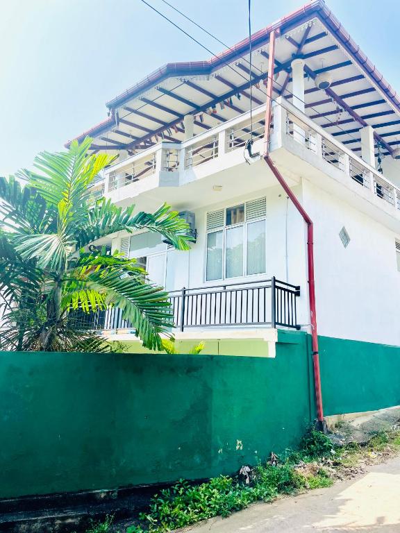 a white house with a green fence and a palm tree at Disna Place in Unawatuna