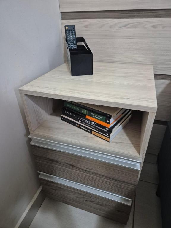 a book shelf with a remote control and a stack of books at Lindo Completíssimo Ap 2 quart Cama King Maq Lavar in Ribeirão Preto