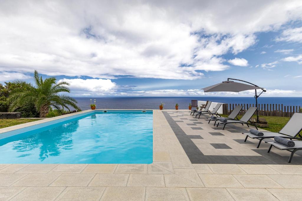 a swimming pool with chairs and a view of the ocean at Grande Mar Villa in Ponta Garça