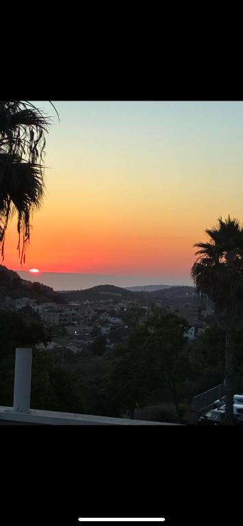 a sunset over a city with a palm tree at קסם גלילי in Ma'alot Tarshiha