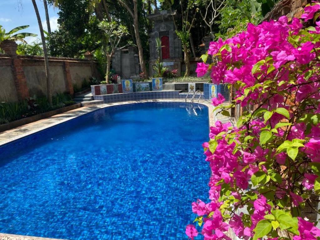 a swimming pool with blue water and purple flowers at Ningmas Escape by Sidhi Hospitality Experiences in Ubud