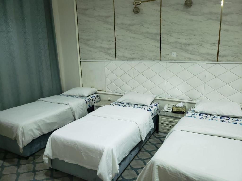 three beds in a room with white sheets at marhaba hotel in Dubai