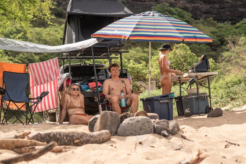 a group of people sitting on the beach under an umbrella at Kauai Explorer Rooftop Camper Drive, Camp & Relax in Anahola