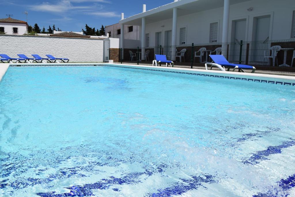 une grande piscine avec des chaises bleues et un bâtiment dans l'établissement Alojamientos Alma, à Conil de la Frontera