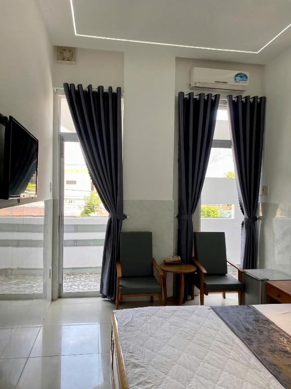 a bedroom with a bed and two chairs and windows at Khách sạn Thảo An in Phước Hậu (1)