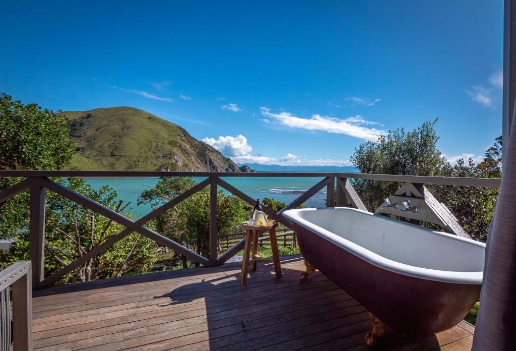 a bath tub on a deck with a view of the ocean at Ngaio Cottage in Cable Bay