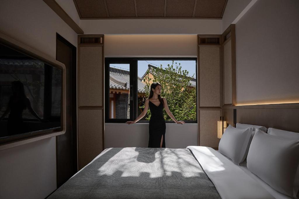 een vrouw in een zwarte jurk die op een raam staat bij Huazhu Luxurious Mountain Courtyard Private Hot Spring Resort in Longmen