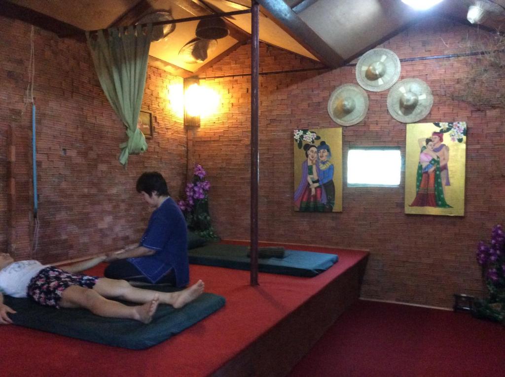 twee mensen zitten op matten in een kamer met schilderijen bij Himawari Restaurant & Cottage in Ban Nong Hin