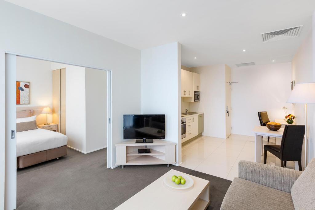 sala de estar con sofá, TV y cama en Oaks Melbourne on Lonsdale Suites, en Melbourne