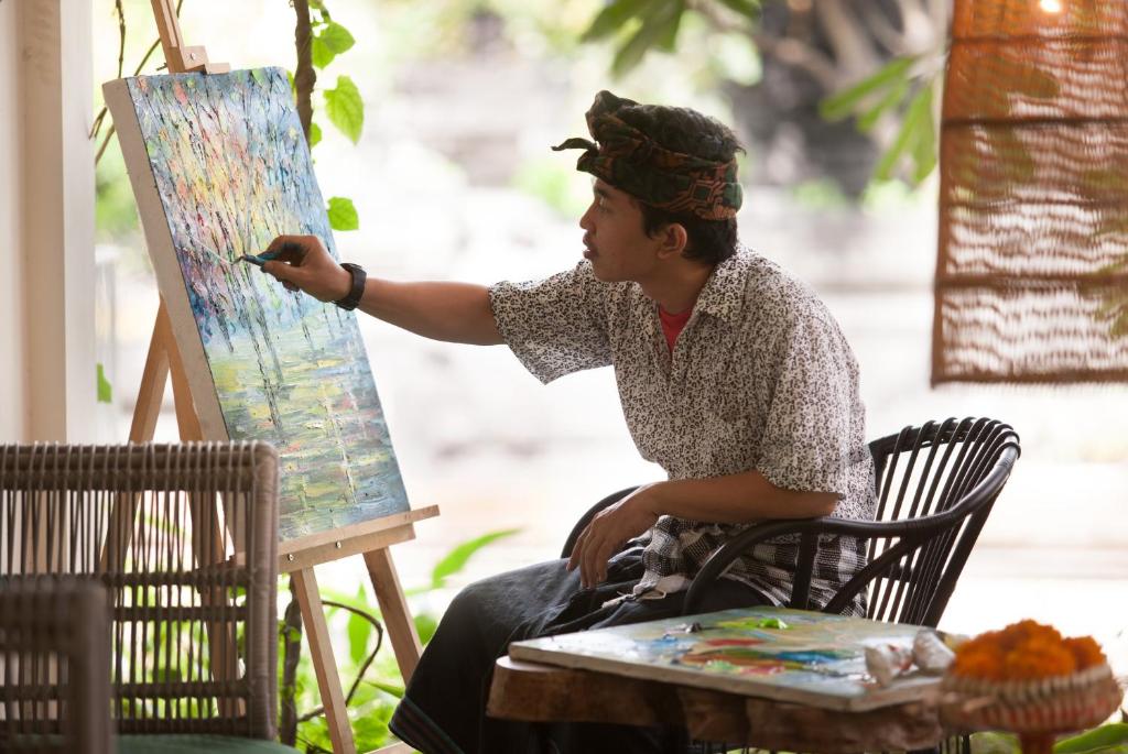 a man sitting in a chair painting a painting at Grandmas Plus Hotel Seminyak in Seminyak