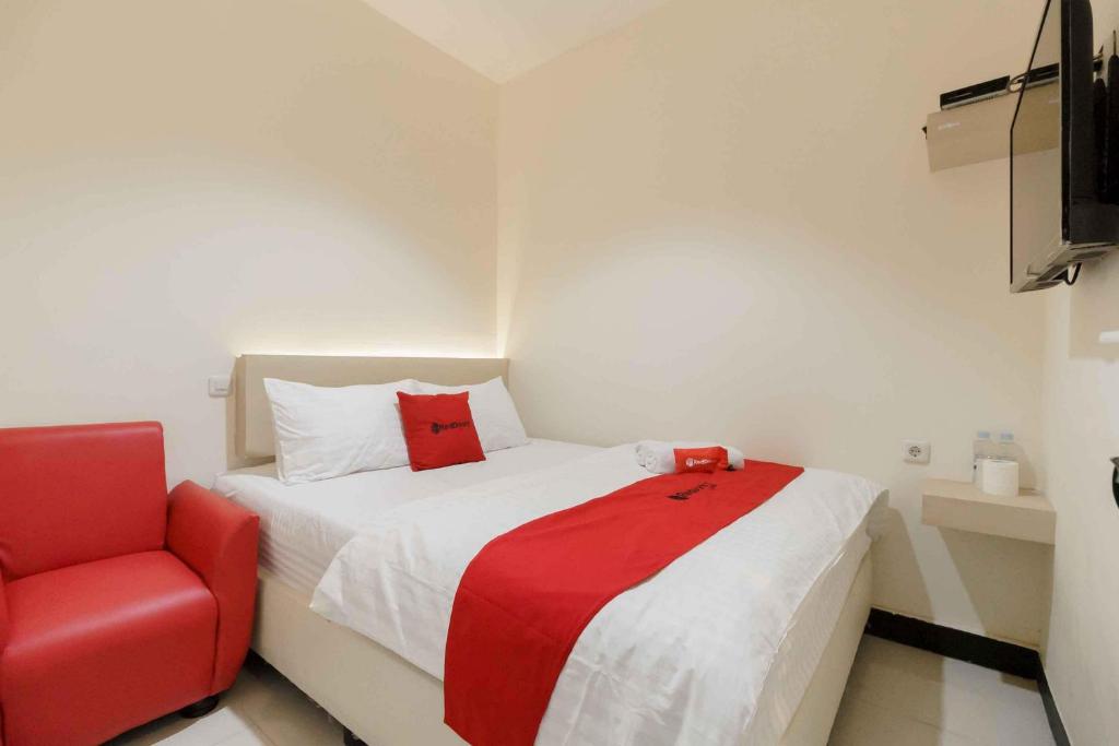 a bedroom with a bed and a red chair at RedDoorz Plus near Millenium ICT Centre Medan 2 in Pulauberayan