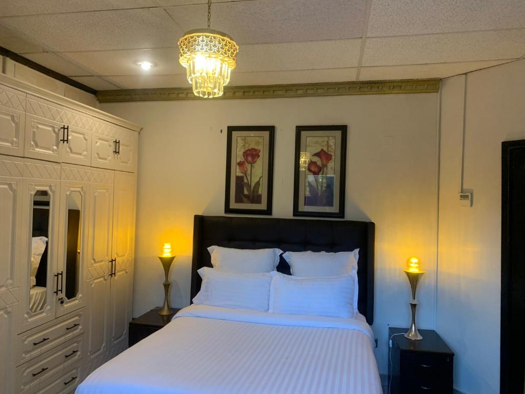 Un dormitorio con una cama con sábanas blancas y una lámpara de araña. en Labelva court Mosi oa tunya, en Lusaka