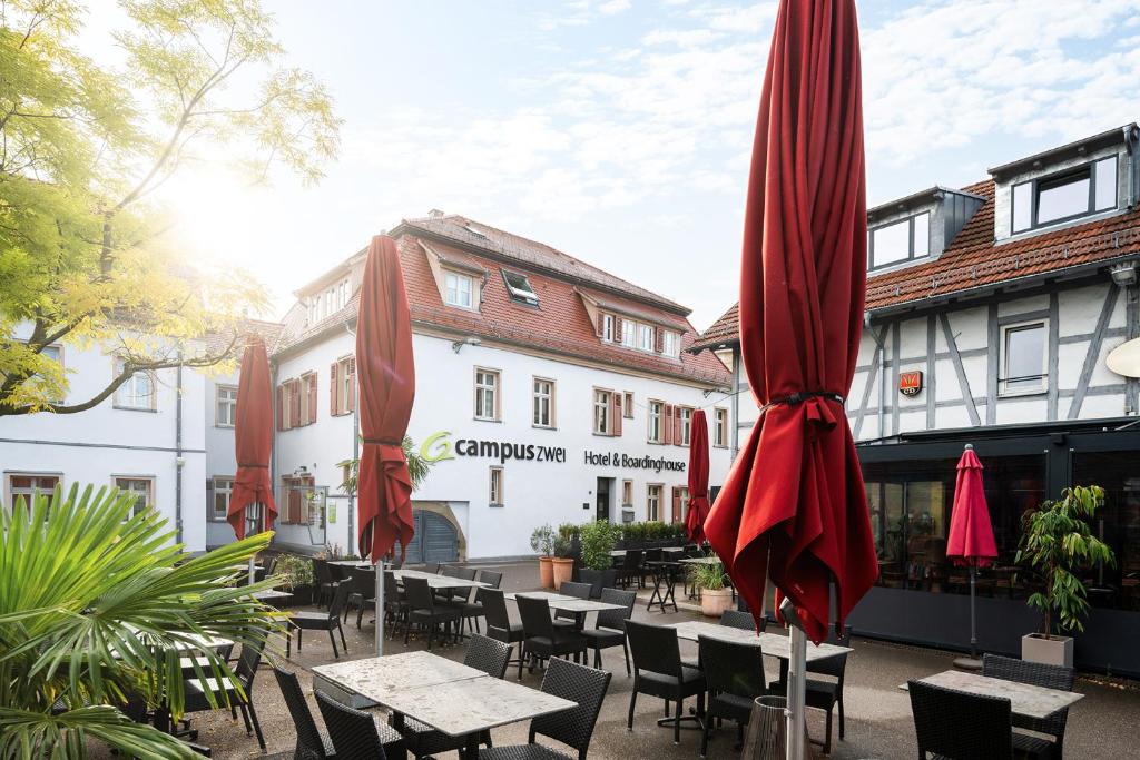 Un grupo de mesas y sombrillas frente a un edificio. en Hotel CampusZwei Komfortable Doppelzimmer &amp; Apartments mit Küche Zentral in Ludwigsburg ideal für Business &amp; Langzeitaufenthalte optional mit Frühstück, en Ludwigsburg