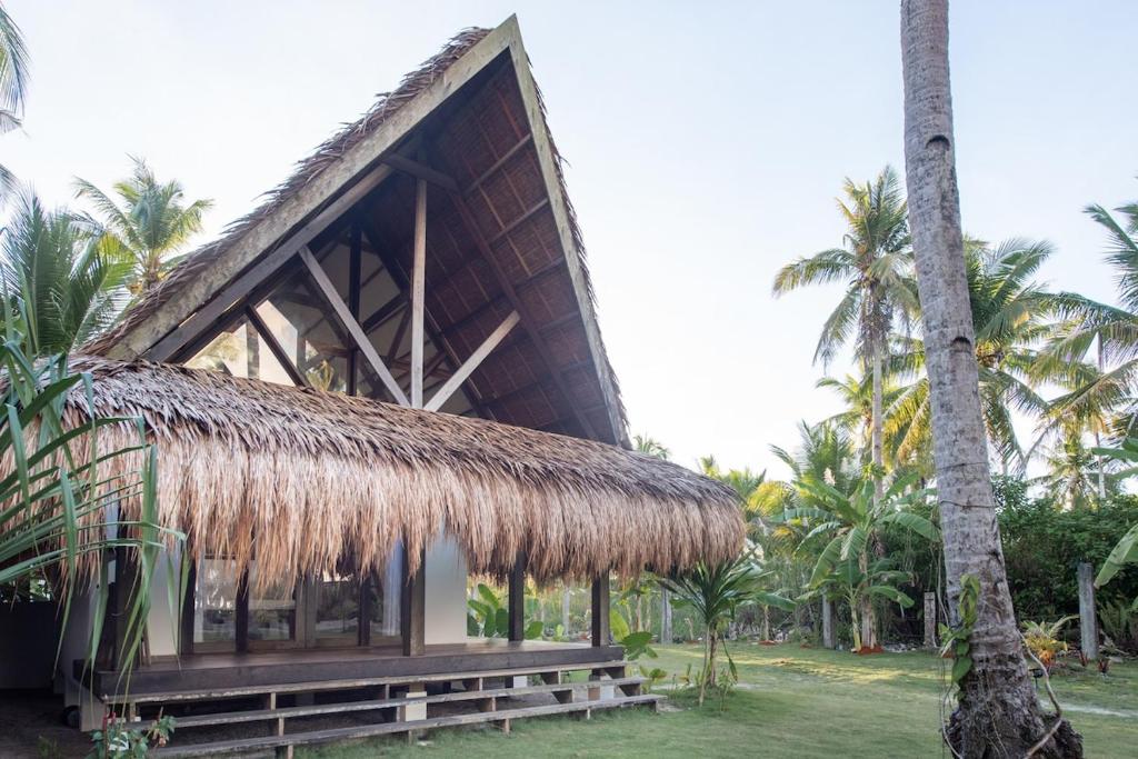 a hut with a straw roof and palm trees at Libertad Surf Villa in General Luna