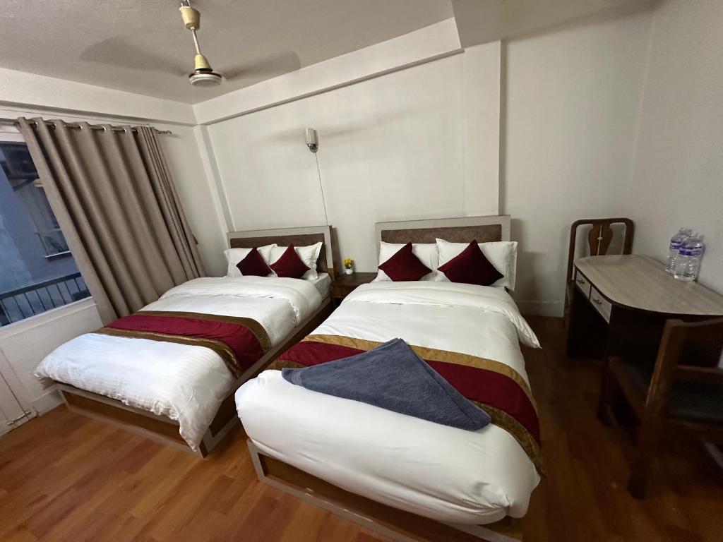 two beds in a room with a table and a window at Om Tara Guest House Pvt Ltd in Kathmandu