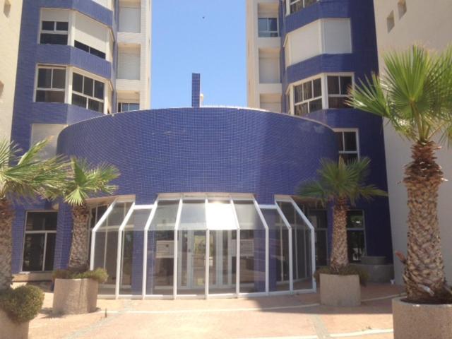 a blue building with palm trees in front of it at Apartment on Nitza 8a in Netanya
