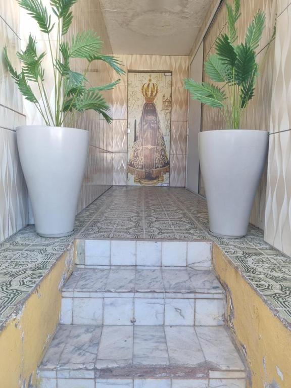 two plants in white pots on a tiled floor at Flat a 4 minutos da basílica in Aparecida