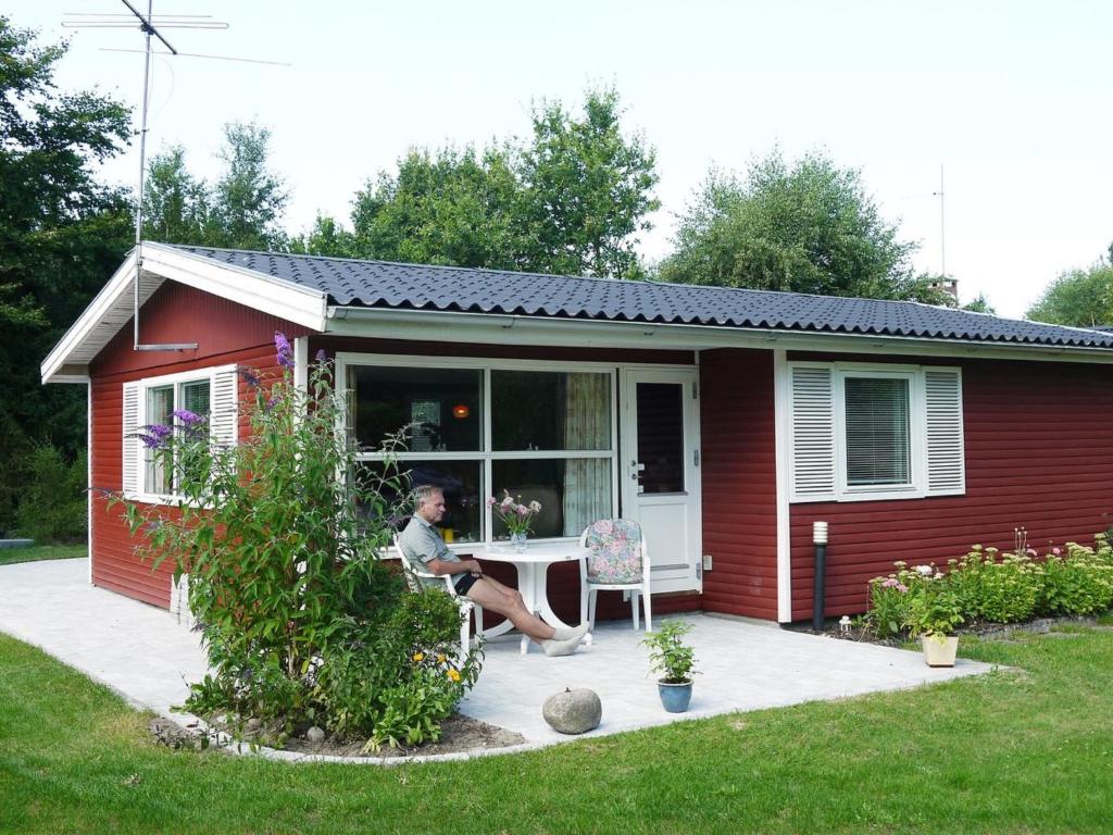 a woman sitting at a table outside of a red house at Holiday Home Desche - 300m from the sea by Interhome in Ørsted