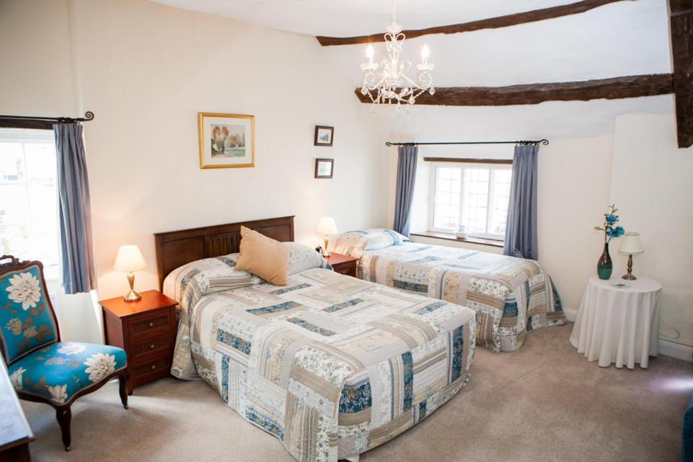 a bedroom with two beds and a chair and a chandelier at Farmhouse Cottage in Sidmouth