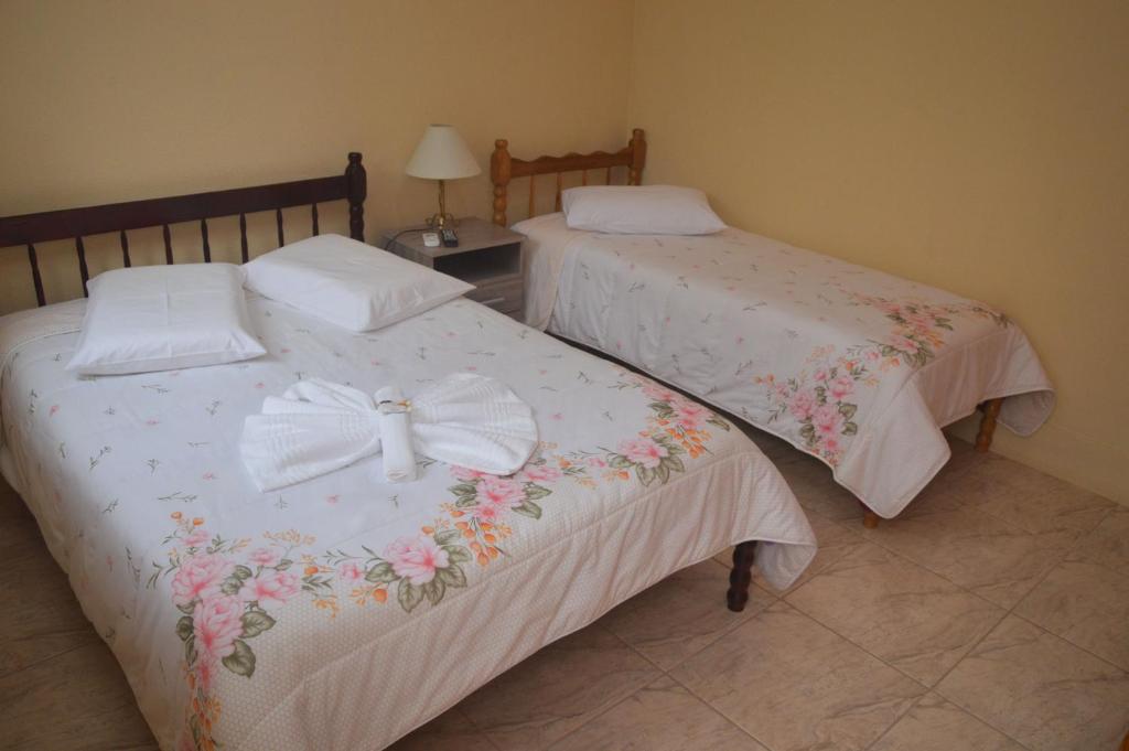 Dos camas con sábanas blancas con flores. en Hotel Fiss, en Morro Redondo