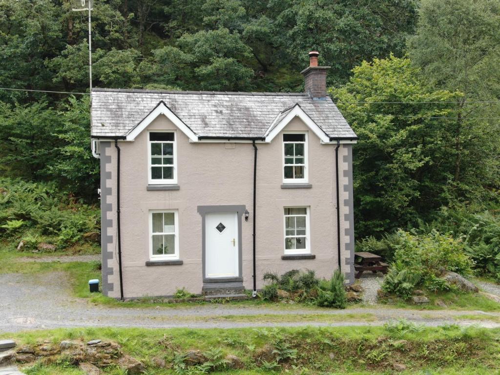 a small house with a white door in the grass at Tan-Y-Garth Cottage Snowdonia in Conwy