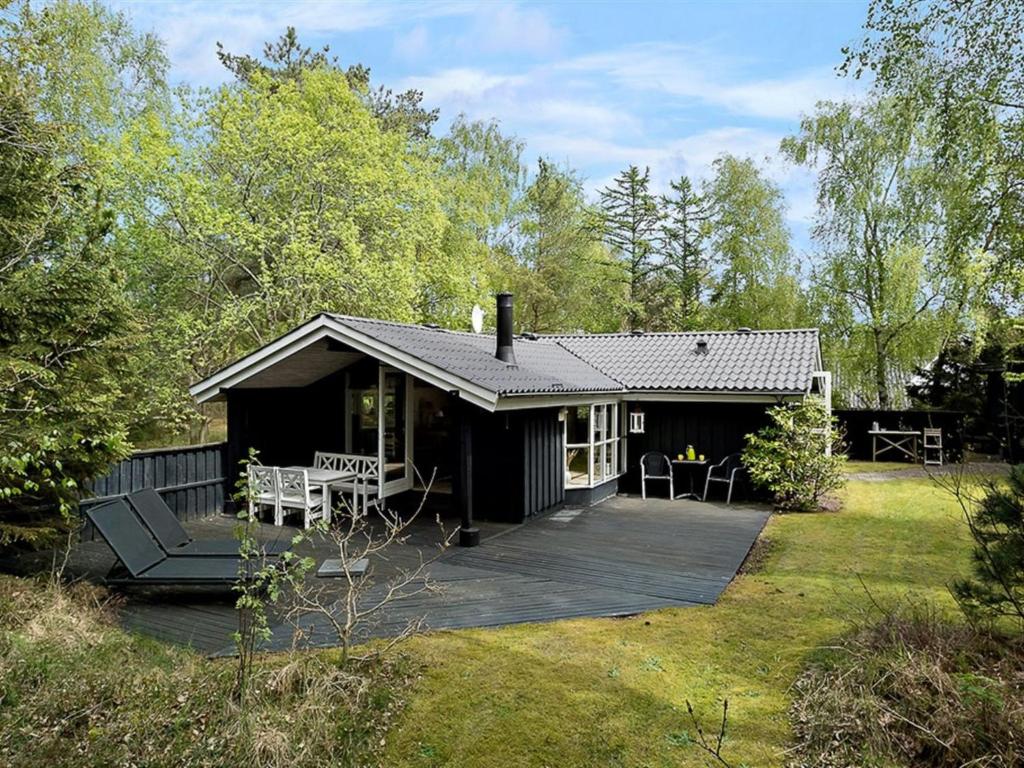 a black cabin with a deck in a yard at Holiday Home Amabel - 200m from the sea by Interhome in Hals