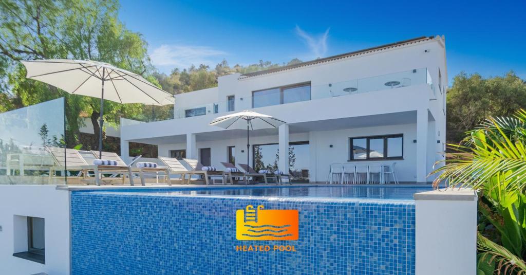 a villa with a swimming pool in front of a house at Happyplace Malaga -- Villa with Panoramic Sea View Heated Infinity Saltwater Pool in Málaga