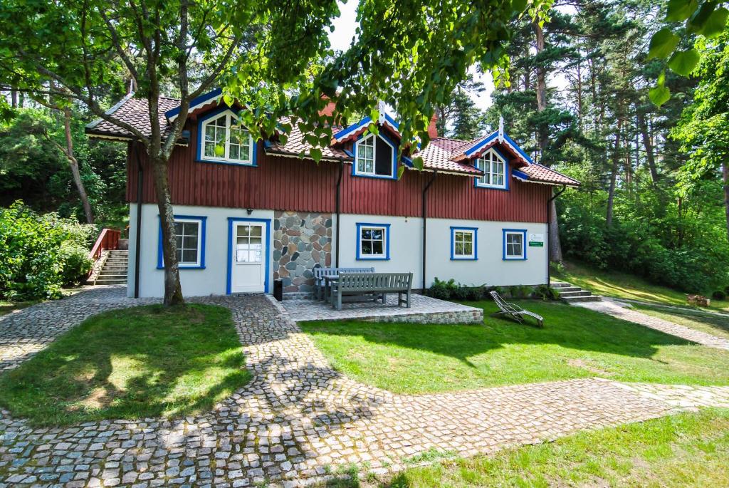 ein rotes und weißes Haus mit einer Bank im Hof in der Unterkunft Apartamentai Geliu Vila in Nida