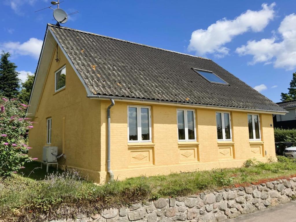 a yellow house with a gray roof and a stone wall at Holiday Home Thessa - 4km from the sea by Interhome in Fåborg