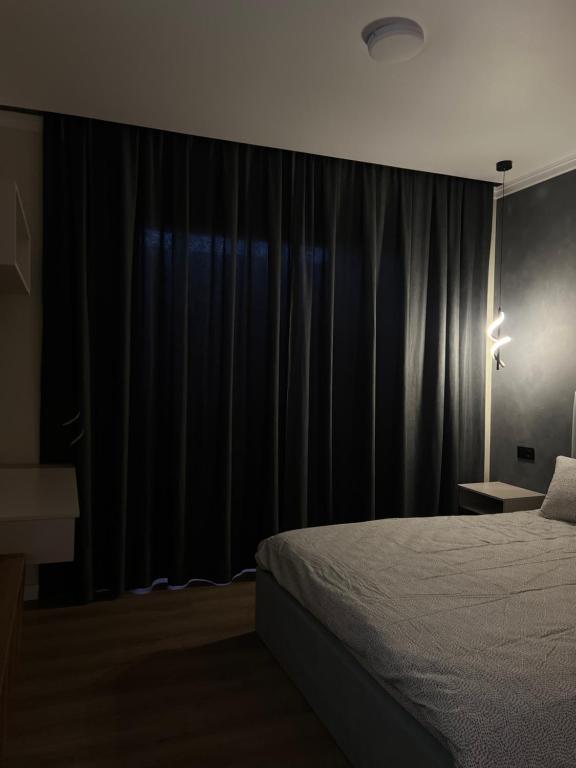 1 dormitorio con 1 cama y una ventana con cortinas negras en Little Comfort Home, en Karakol