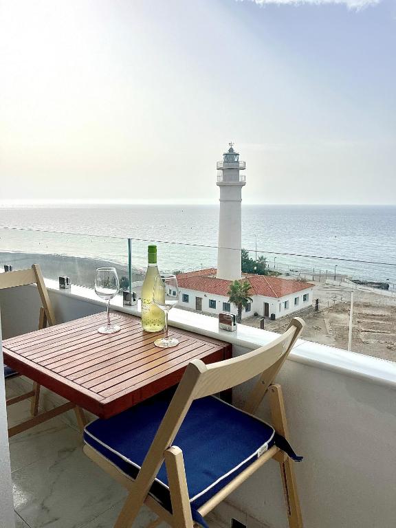 a table with two wine glasses and a lighthouse at Primera linea de playa en Torrox Costa in Torrox Costa