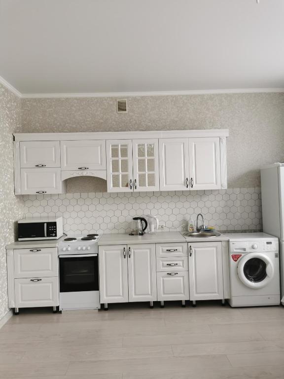 une cuisine avec des armoires blanches, un évier et un lave-vaisselle dans l'établissement 2х комнатная студия в центре, новый дом, à Kostanay