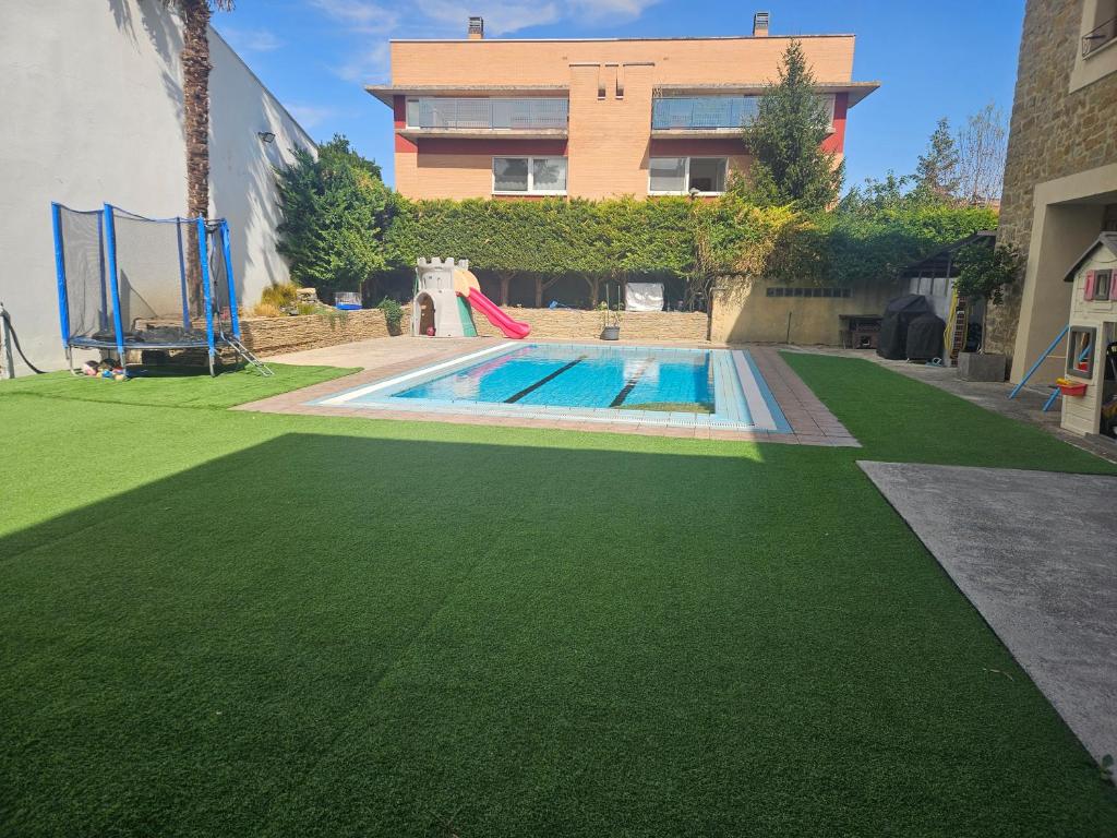 a swimming pool with green grass next to a house at Descanso urbano Pamplona in Mutilva Alta