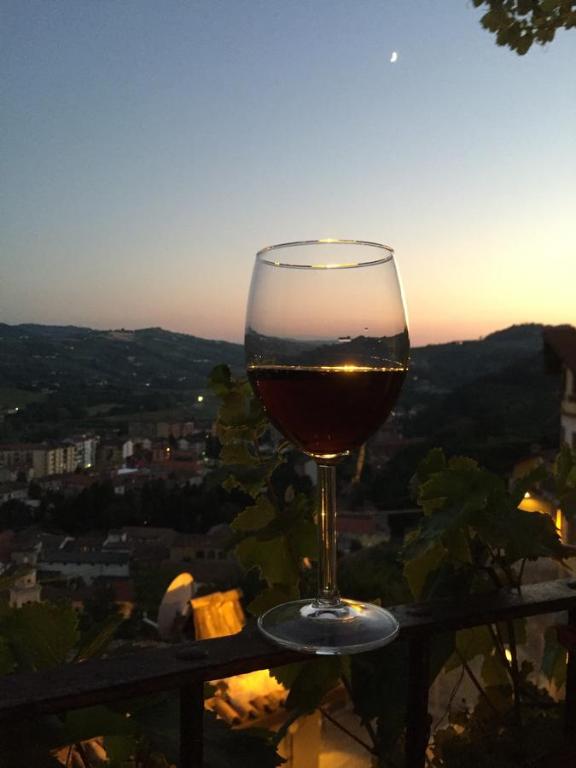 Ein Glas Wein, auf einem Geländer sitzend, während der Sonnenuntergang genossen wird in der Unterkunft View & Wine Room in Canelli