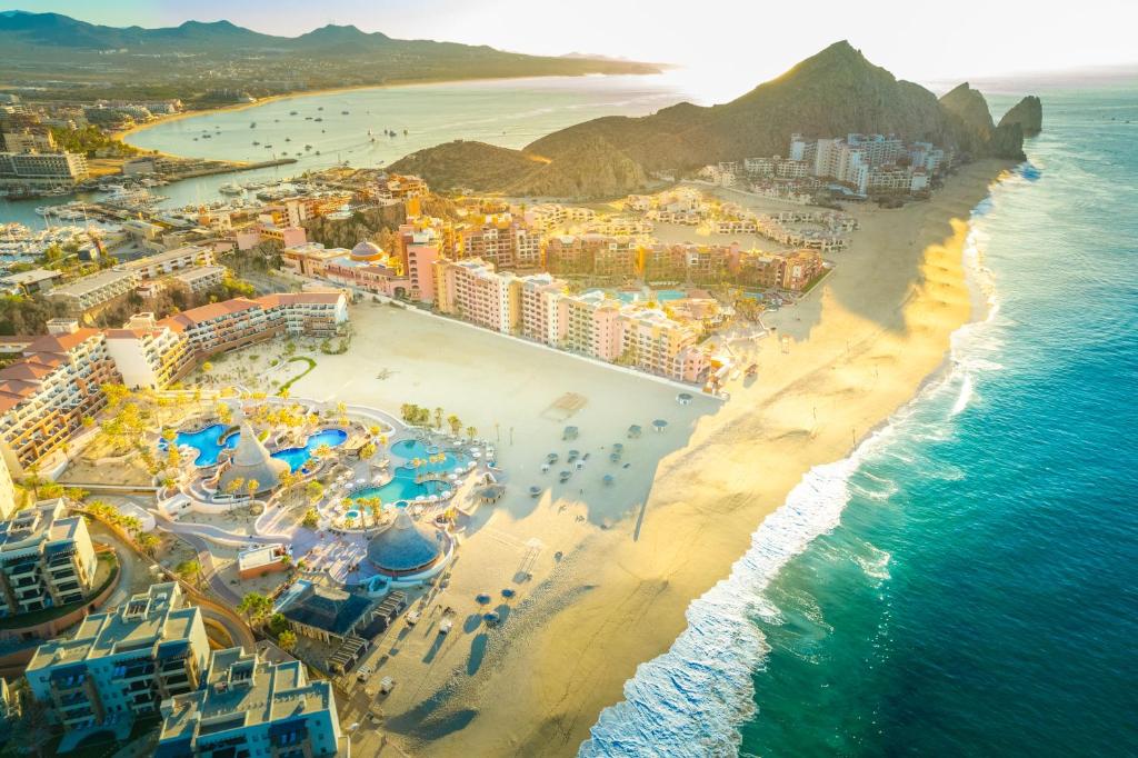Aerial view of beachfront resort with multiple pools, hotels, and sandy beach along coastline.