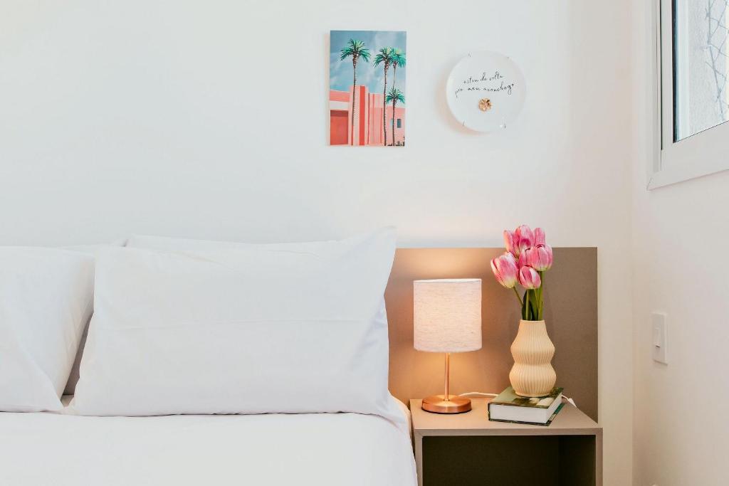 イタパリカにある2Q moderno c/ Piscina e Academiaのベッドと花瓶が置かれたテーブルのある寝室